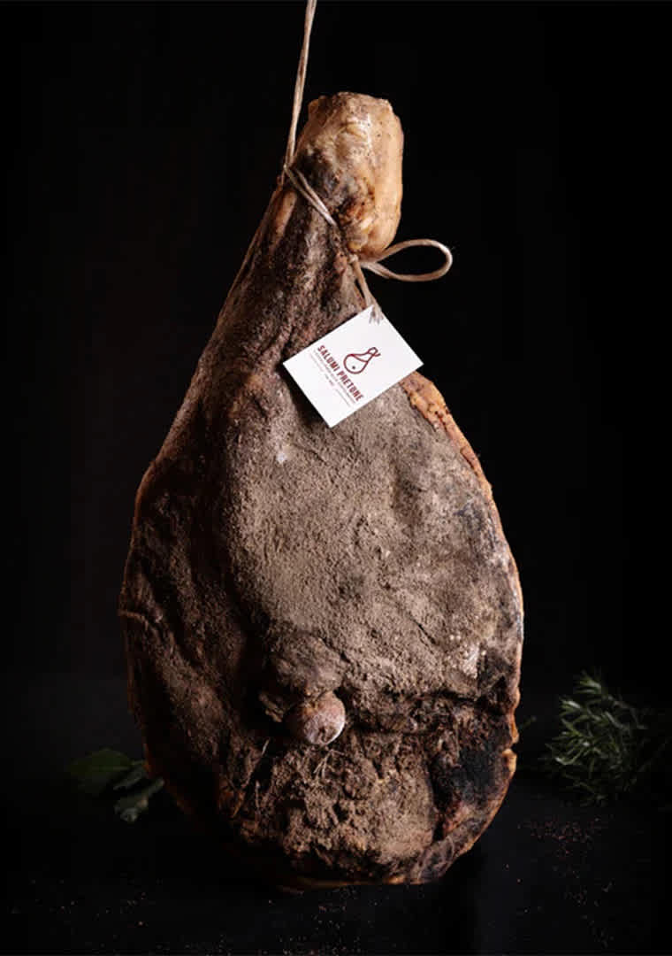 Prosciutto_intero_di_suino_nero_brado_salume_artigianale_umbro_Salumi_Pretone_su_sfondo_nero_con_erb